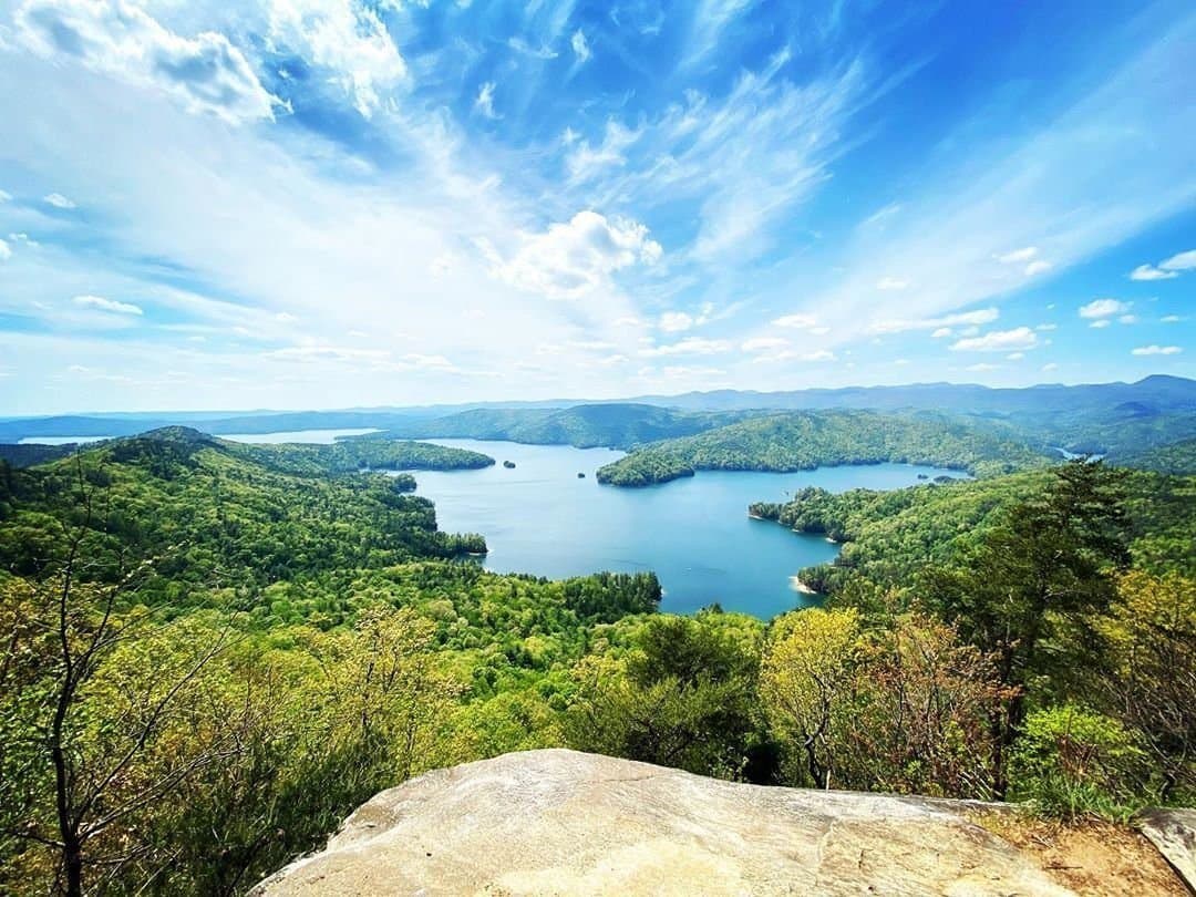 Blue lake water winding between forested ridges under a bright sky, seen from a rock overlook — photography from the Jocassee Medspa site